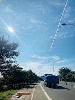 A tractor trailer driving along a highway under a bright sky.