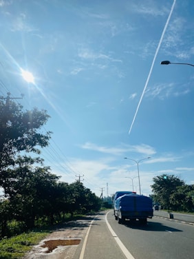 A modern cargo truck driving on a highway surrounded by green fields under a clear blue sky.