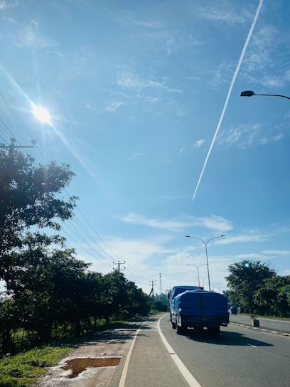 A modern cargo truck driving on a highway surrounded by green fields under a clear blue sky.