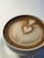A cup of coffee with intricate latte art featuring two hearts poured into the foam, set on a white saucer against a light-colored background.