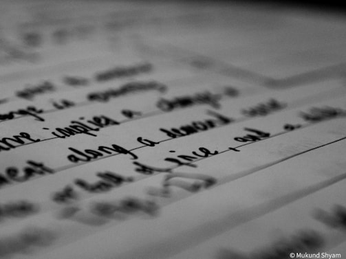 A close-up view of handwritten text on a piece of paper, captured in black and white. The emphasis is on the script, with some areas blurred, likely due to depth of field.
