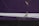A close-up of a wall with significant cracks in the purple paint. The wall features a white horizontal stripe in the middle. There are patches where the paint is peeling off, revealing a beige color underneath.