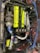 A detailed view of a car engine with a prominent neon yellow cover labeled 'Twin Cam 16 Super Charger' and 'Toyota'. Surrounding this are various components, including a turbocharger, hoses, and wires. There are several branded parts, such as a blue intake pipe with 'Ultra Racing' printed on it.