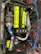 A detailed view of a car engine with a prominent neon yellow cover labeled 'Twin Cam 16 Super Charger' and 'Toyota'. Surrounding this are various components, including a turbocharger, hoses, and wires. There are several branded parts, such as a blue intake pipe with 'Ultra Racing' printed on it.