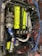 A detailed view of a car engine with a prominent neon yellow cover labeled 'Twin Cam 16 Super Charger' and 'Toyota'. Surrounding this are various components, including a turbocharger, hoses, and wires. There are several branded parts, such as a blue intake pipe with 'Ultra Racing' printed on it.