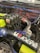 A close-up view of a car engine with visible components including ignition coils marked with 'Bosch Coil', various pipes, and wires. There is a prominent black air intake tube with 'Ultra Racing' branding and colorful wires in blue and yellow. A metallic pipe featuring a red connector is also visible.