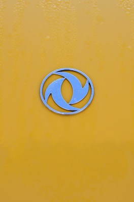 Golden æ symbol badge on a dark blue metallic background with soft glowing edges.