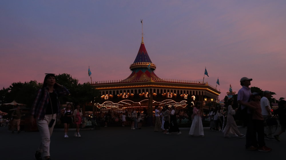 a crowd of people standing around a carousel at dusk