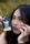 A close-up of a person holding a tarot card labeled 'The Moon' next to their face. The person has celestial symbols like crescent moons and stars drawn around their eyes and forehead. They have black nail polish and long dark hair, and their expression is thoughtful and enigmatic.