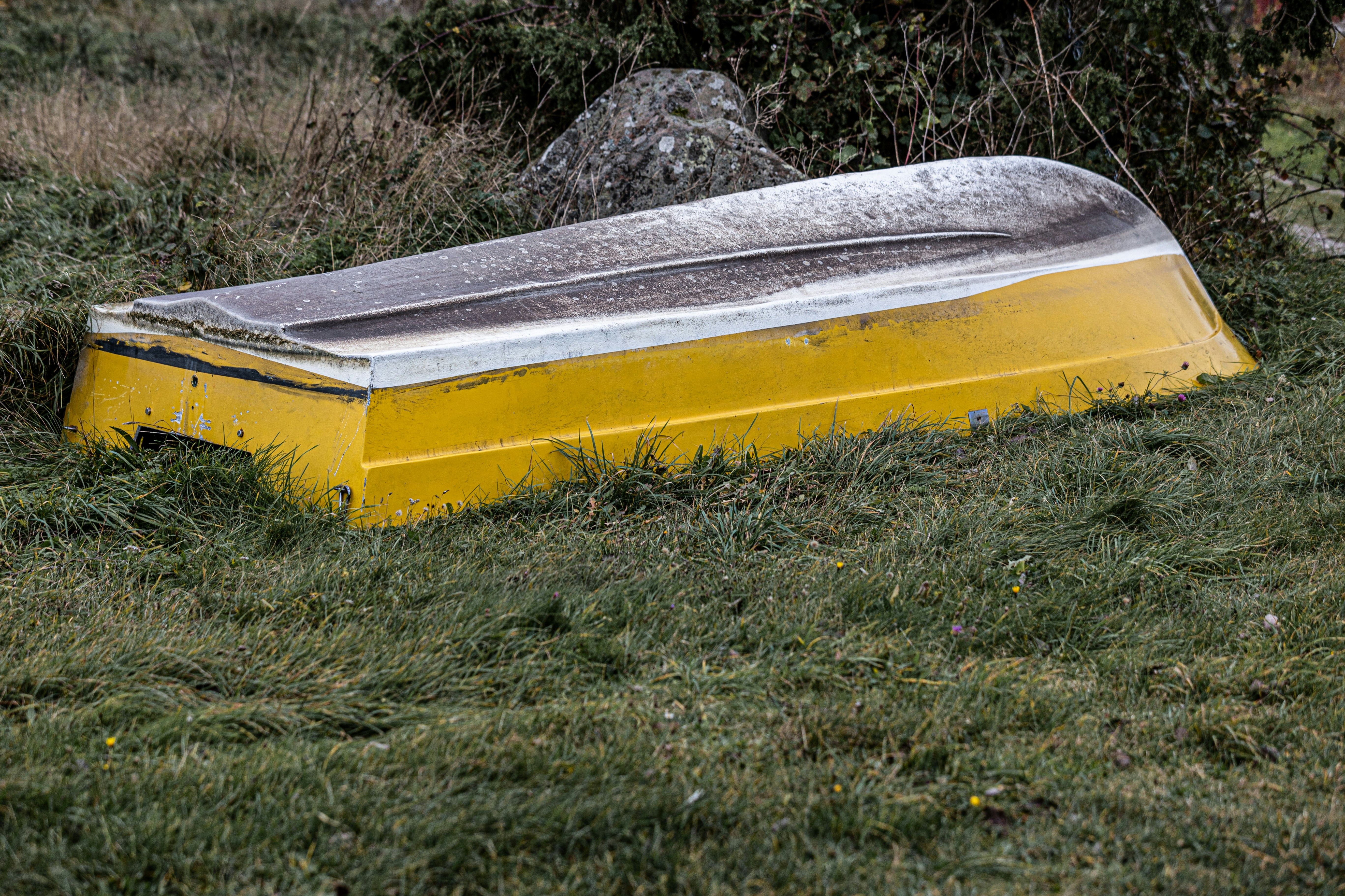a yellow and silver boat sitting in the grass, A yellow rowing boat lying upside down in the grass.