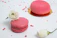 Close-up of a delicate pastel pink macaron with gold dust on a cream background.