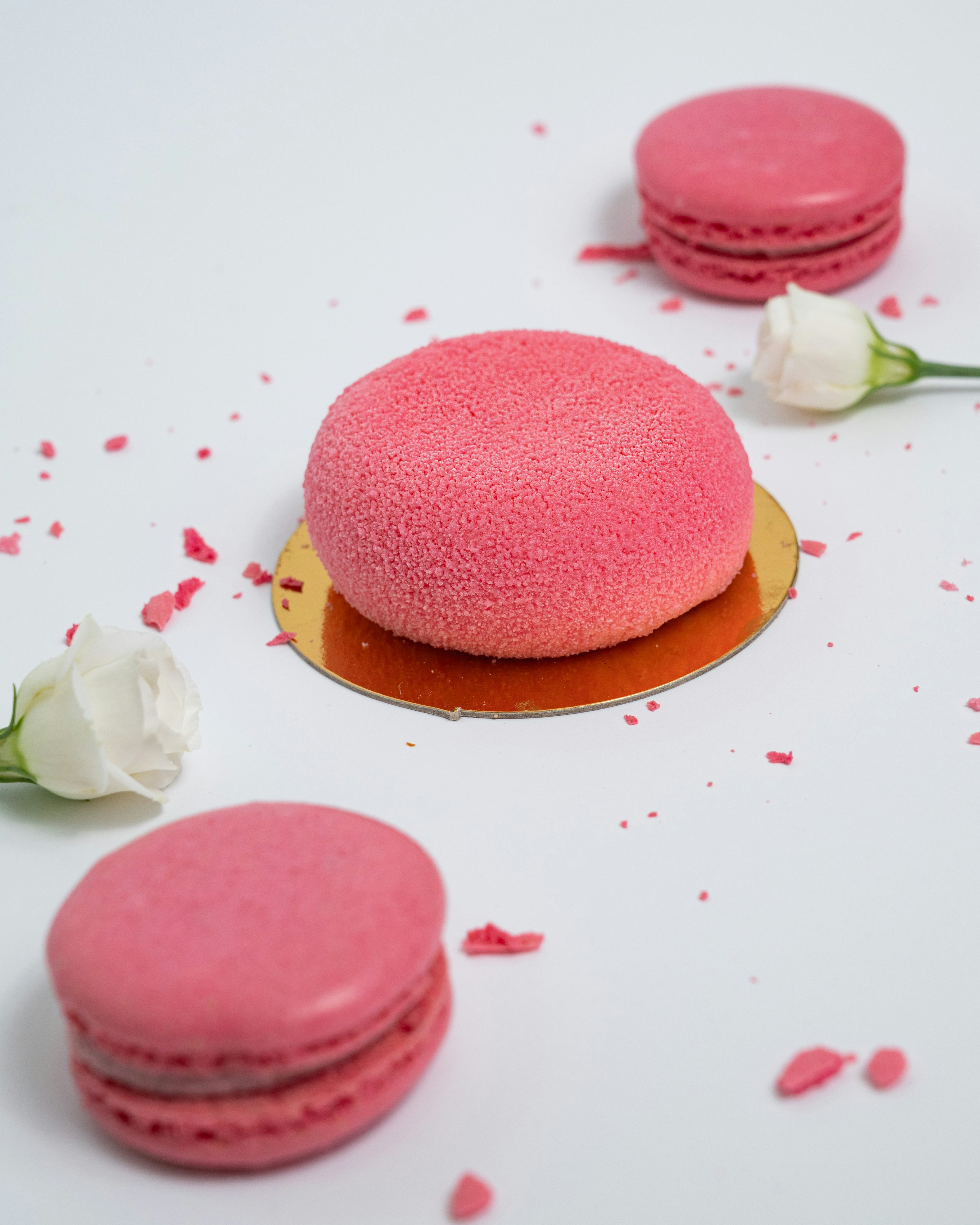 three pink macaroons on a white table with rose petals