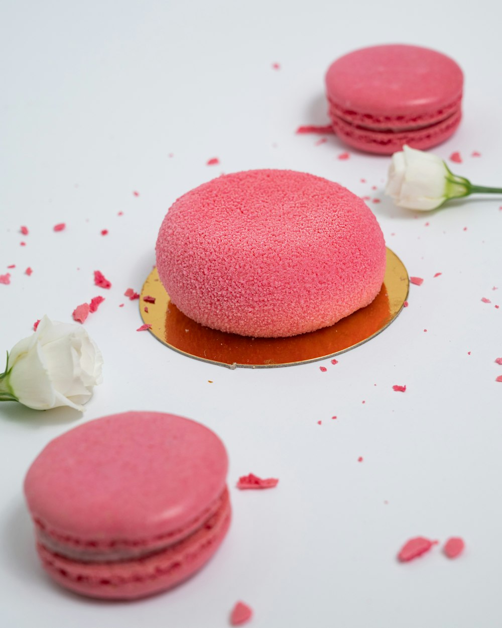 three pink macaroons on a white table with rose petals