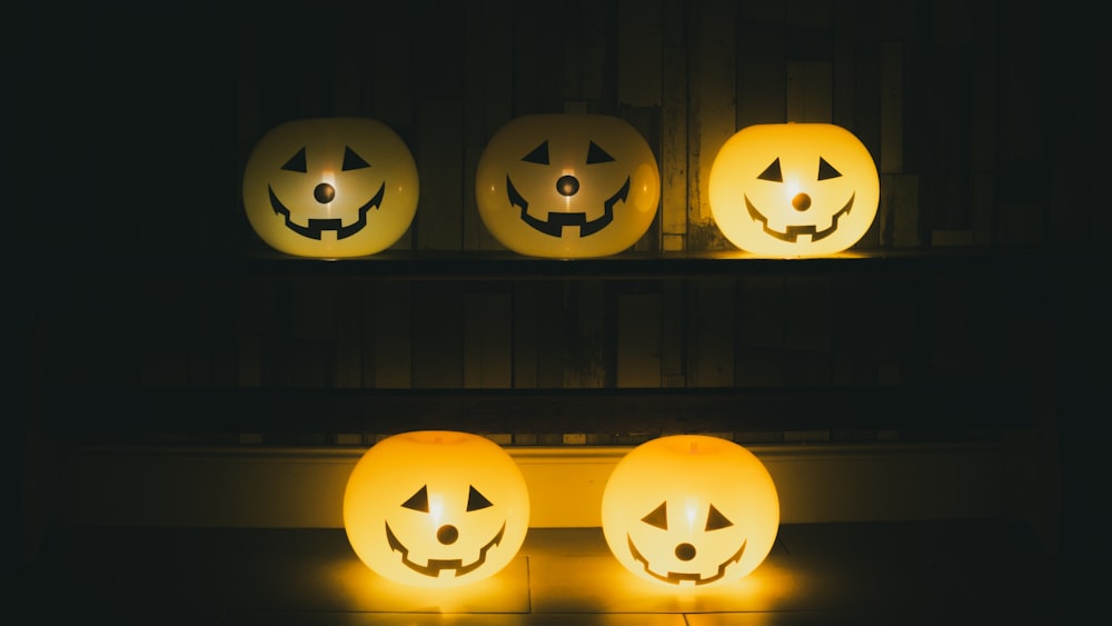 three lighted pumpkins sitting on a shelf in the dark