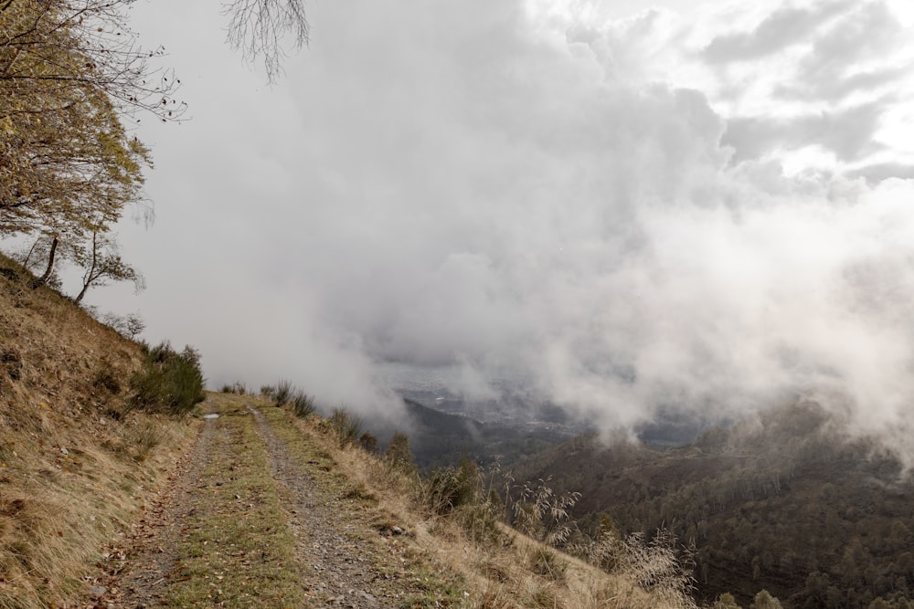 a dirt road going up a hill with clouds in the background