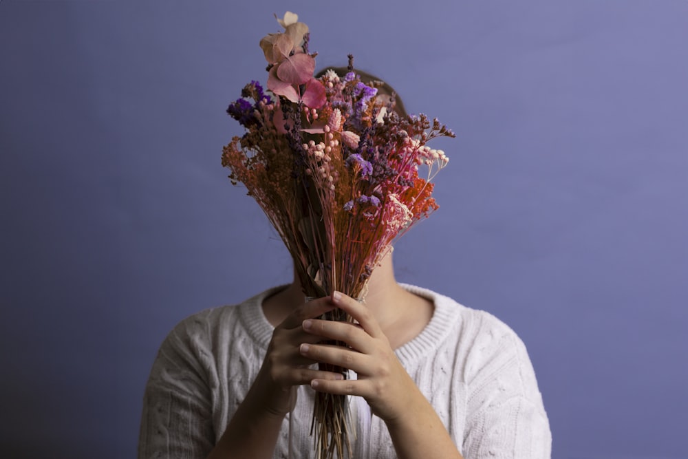 a woman holding a bunch of dried flowers