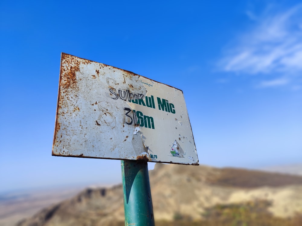 a rusted sign on a metal pole with a mountain in the background