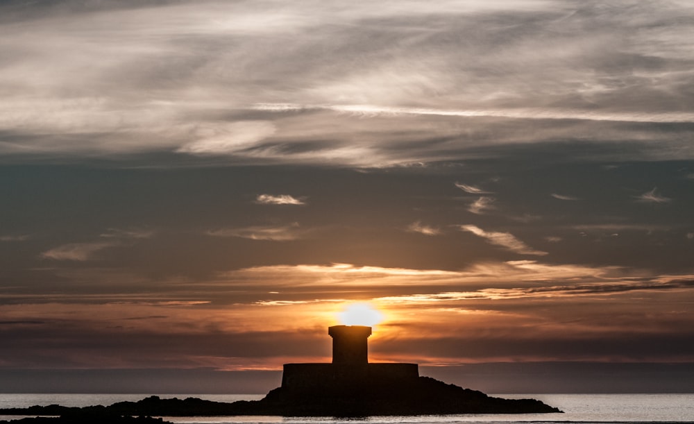 the sun is setting behind a lighthouse on a small island