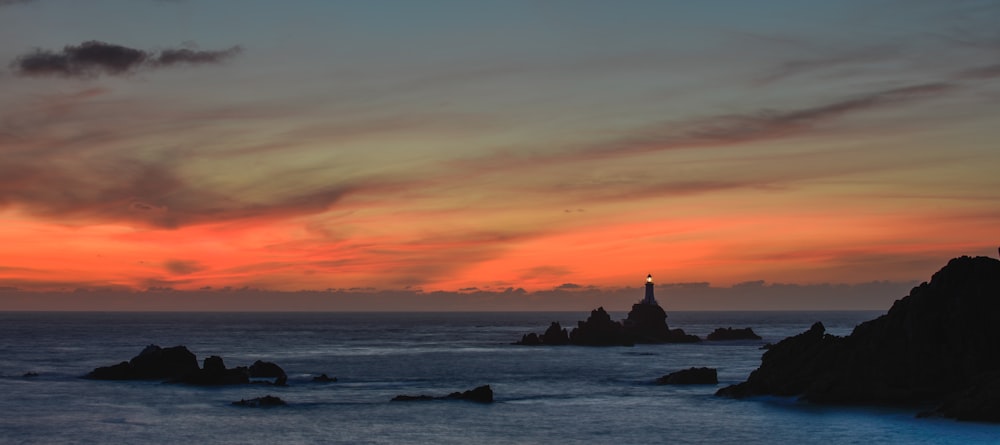 Ein Sonnenuntergang über dem Meer mit einem Leuchtturm in der Ferne