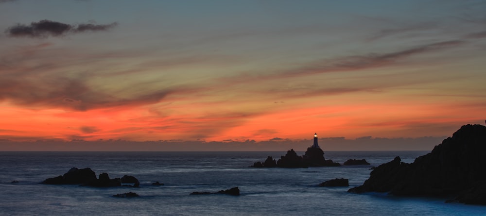 a sunset over the ocean with a lighthouse in the distance