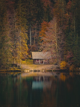 Cozy wooden mountain lodge nestled among autumn-colored trees beside a calm lake