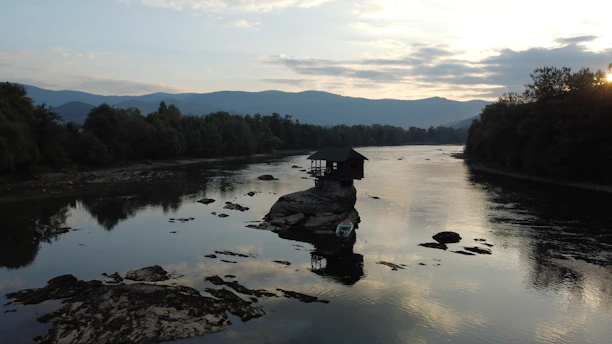 A cozy wooden homestay nestled beside a flowing mountain river at sunset in Himachal Pradesh.
