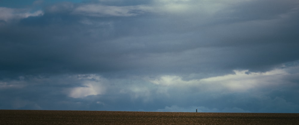 a lone person walking across a field under a cloudy sky