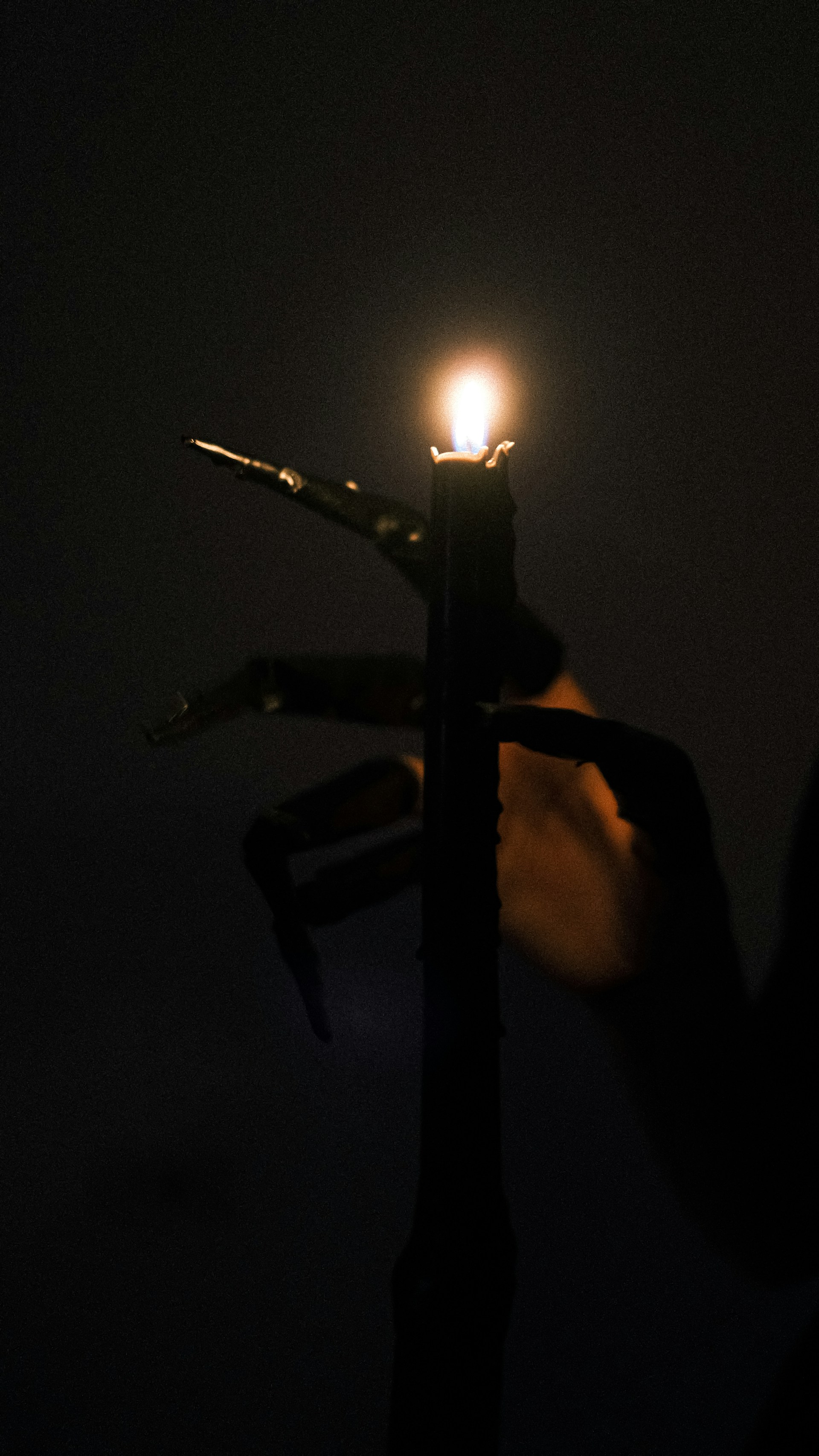 A hauntingly beautiful still from an indie horror film, featuring a shadowy figure framed by flickering candlelight against a textured, darkened backdrop.