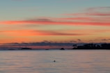 Sunset over the calm sea with silhouettes of islands in the distance.