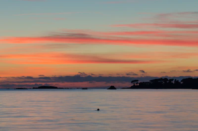 Sunset view over the calm sea with silhouettes of islands in the distance.