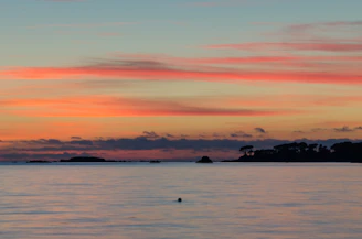 Sunset view over the calm sea with silhouettes of islands in the distance.