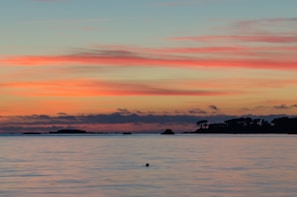 Sunset over the calm sea with silhouettes of islands in the distance.