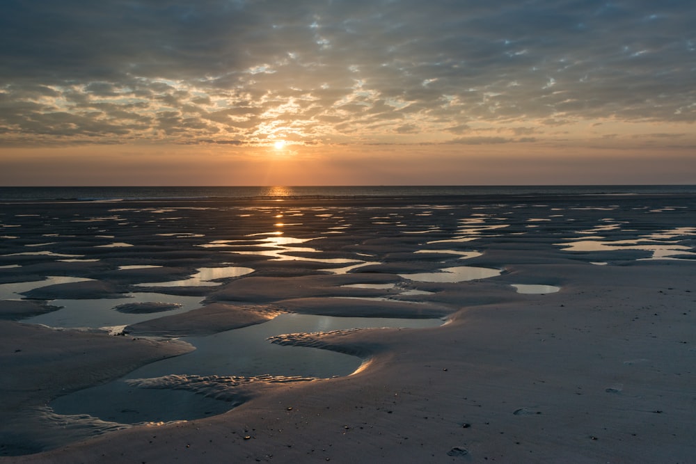 the sun is setting over the water on the beach