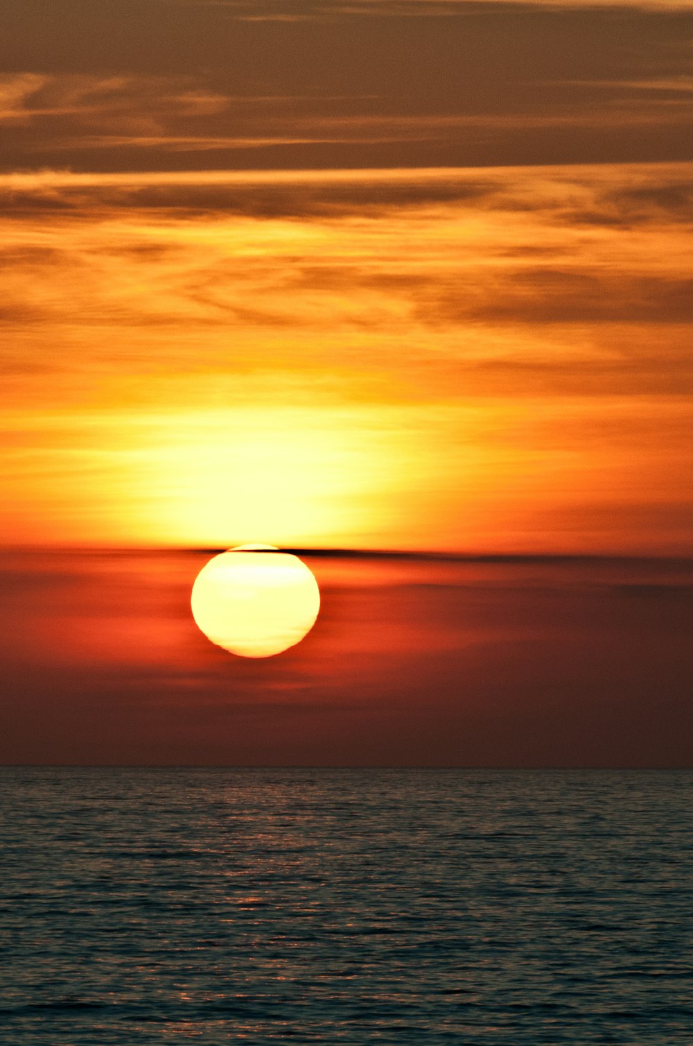 the sun is setting over the ocean on a cloudy day