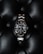 A luxury watch with a stainless steel bracelet and black dial is prominently displayed on a textured black leather surface. The watch face features luminous hour markers, a date window, and a rotating bezel marked with numerals.