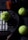 A padel racket lies on a dark surface, accompanied by three bright yellow padel balls. The balls are scattered around the racket, which has a circular grid design with large holes. A cylindrical container with an orange lid, likely a ball canister, is partially visible.