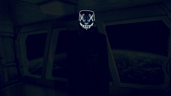 A dark, futuristic room with an individual wearing a hooded cloak and a glowing mask with crossed eyes and a stitched mouth design. The background features large windows displaying a view of Earth from space, creating an eerie and mysterious atmosphere.