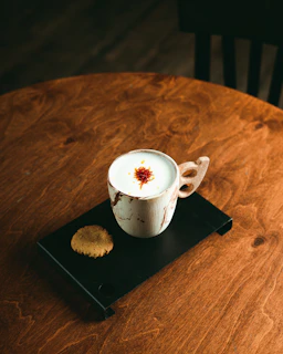 A steaming cup of masala chai with a side of almond biscotti on a rustic wooden table.