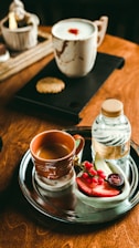 A cozy café table with a cup of black coffee, a fresh fruit juice, and a sandwich on a wooden tray.