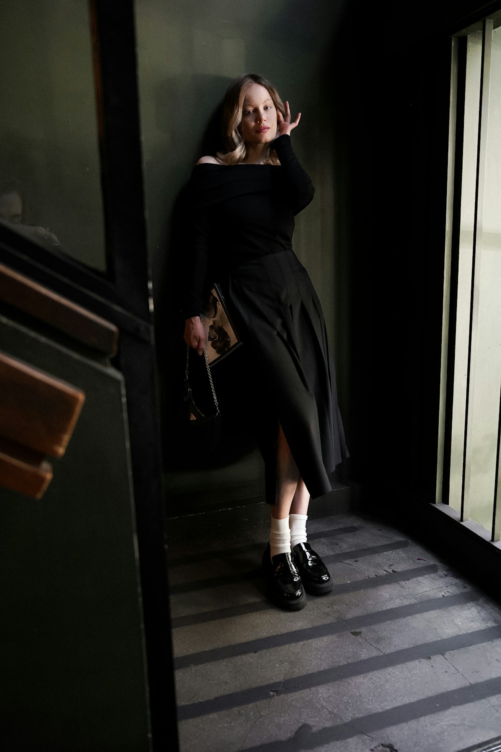 a woman in a black dress leaning against a wall