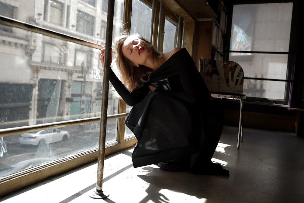 a woman in a black dress leaning against a window