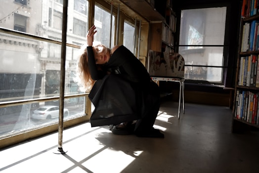 A contemplative poet seated in a minimalist room with soft shadows and warm light, surrounded by books and a microphone.