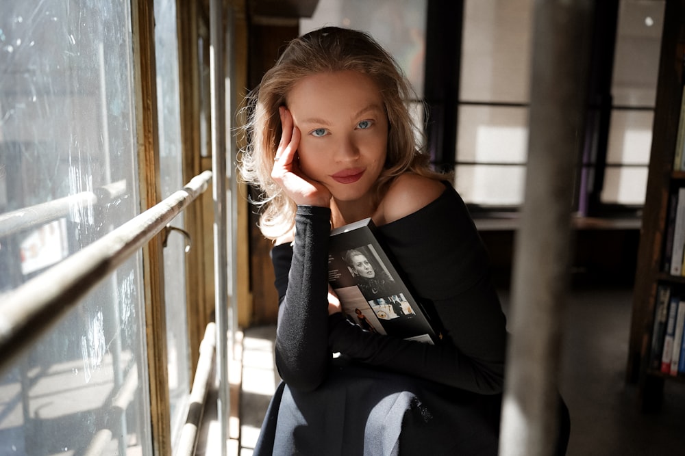 a woman leaning against a window with a book in her hand