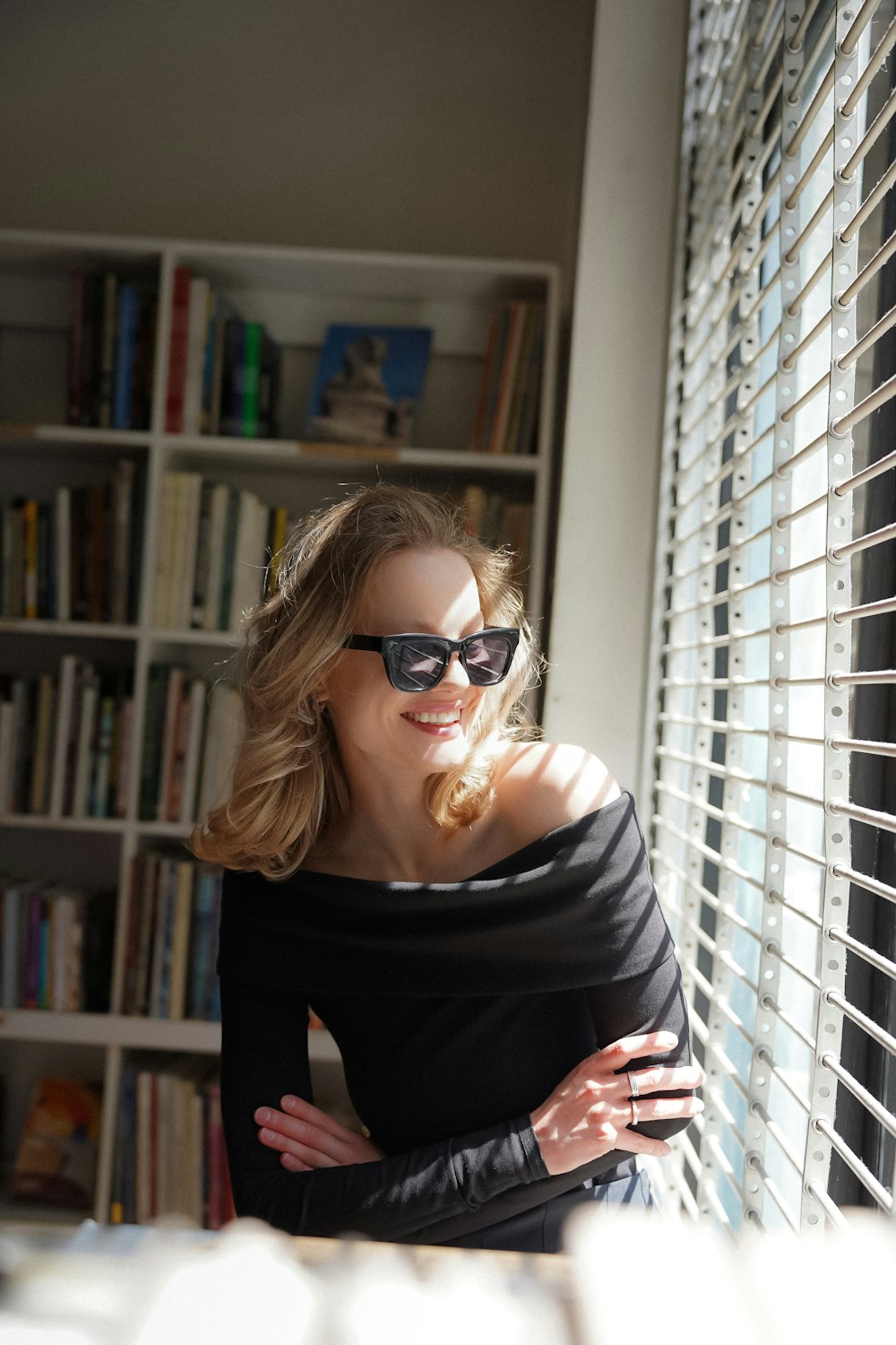 une femme vêtue d’un haut noir et de lunettes de soleil regardant par la fenêtre