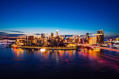 City skyline at dusk with glowing lights reflecting on the river.