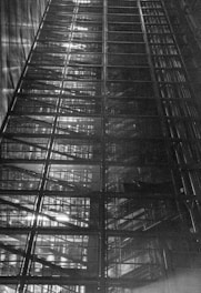 A dramatic upward view of a large, industrial metal structure with multiple layers and intricate patterns, displaying lines and grids with light filtering through sections.