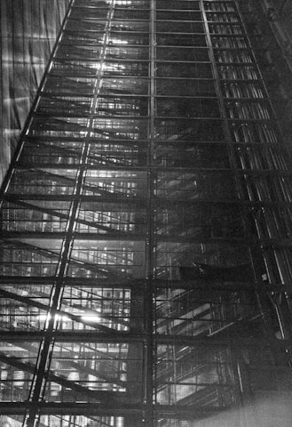 A dramatic upward view of a large, industrial metal structure with multiple layers and intricate patterns, displaying lines and grids with light filtering through sections.