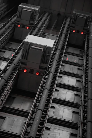 A sleek, industrial-style photo of elevator electrical components arranged on a dark navy background with bold red accents.