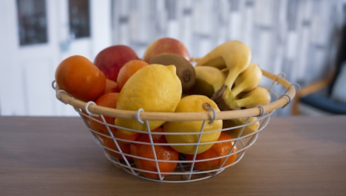 A cheerful basket overflowing with fresh bananas and other fruits on a wooden table.