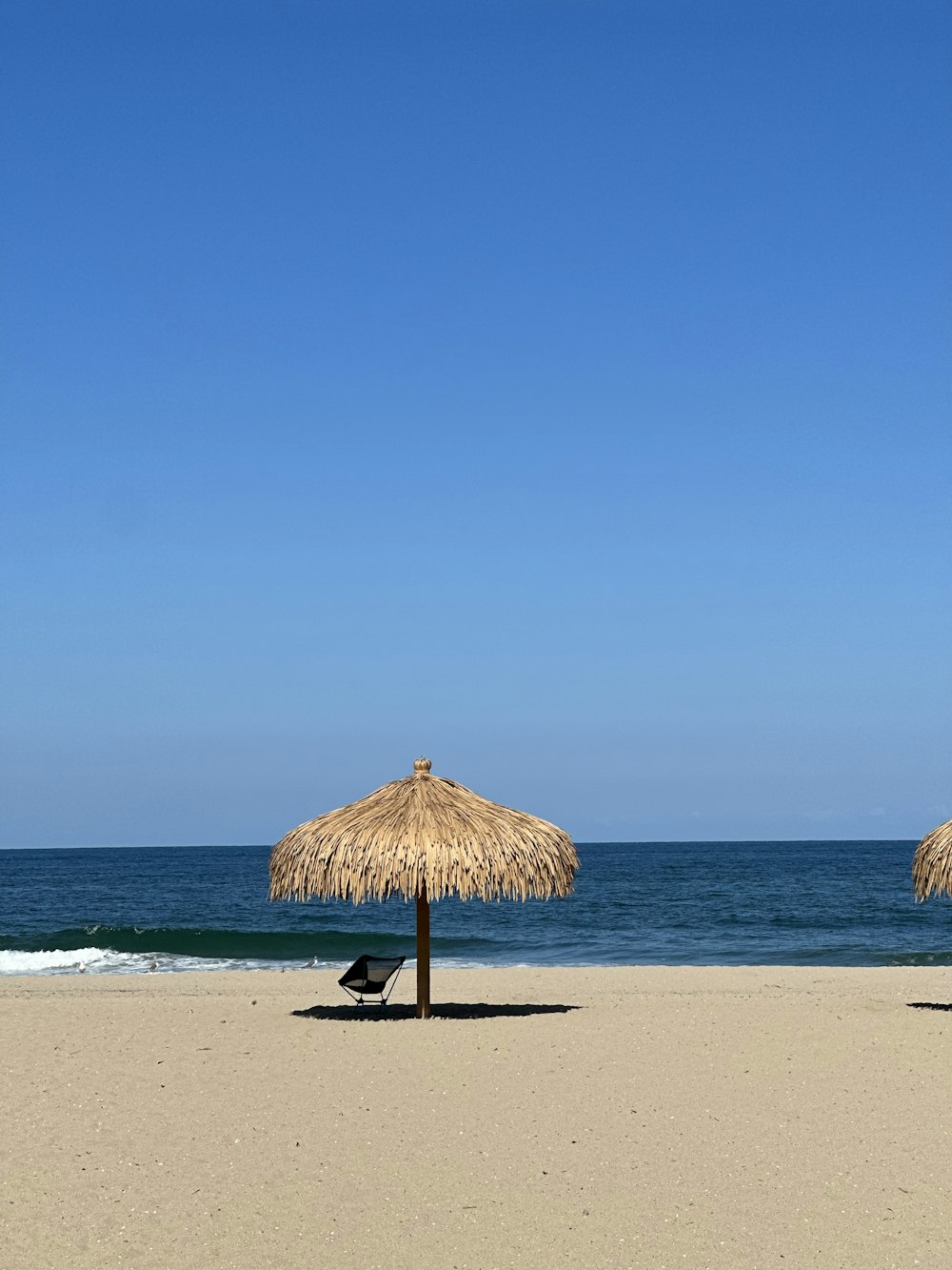 two straw umbrellas sitting on top of a sandy beach